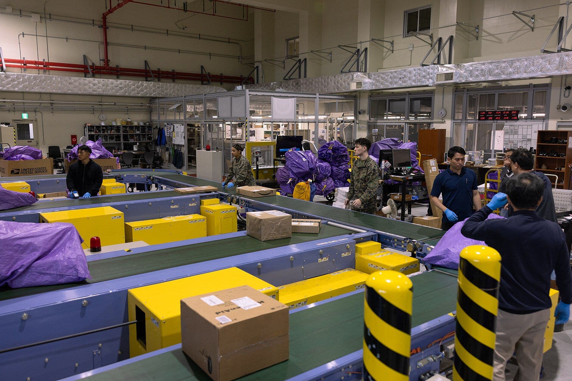 Bir dağıtım merkezinde konveyör hatları üzerinde ilerleyen koliler ve paketleri ayıran çalışanlar.