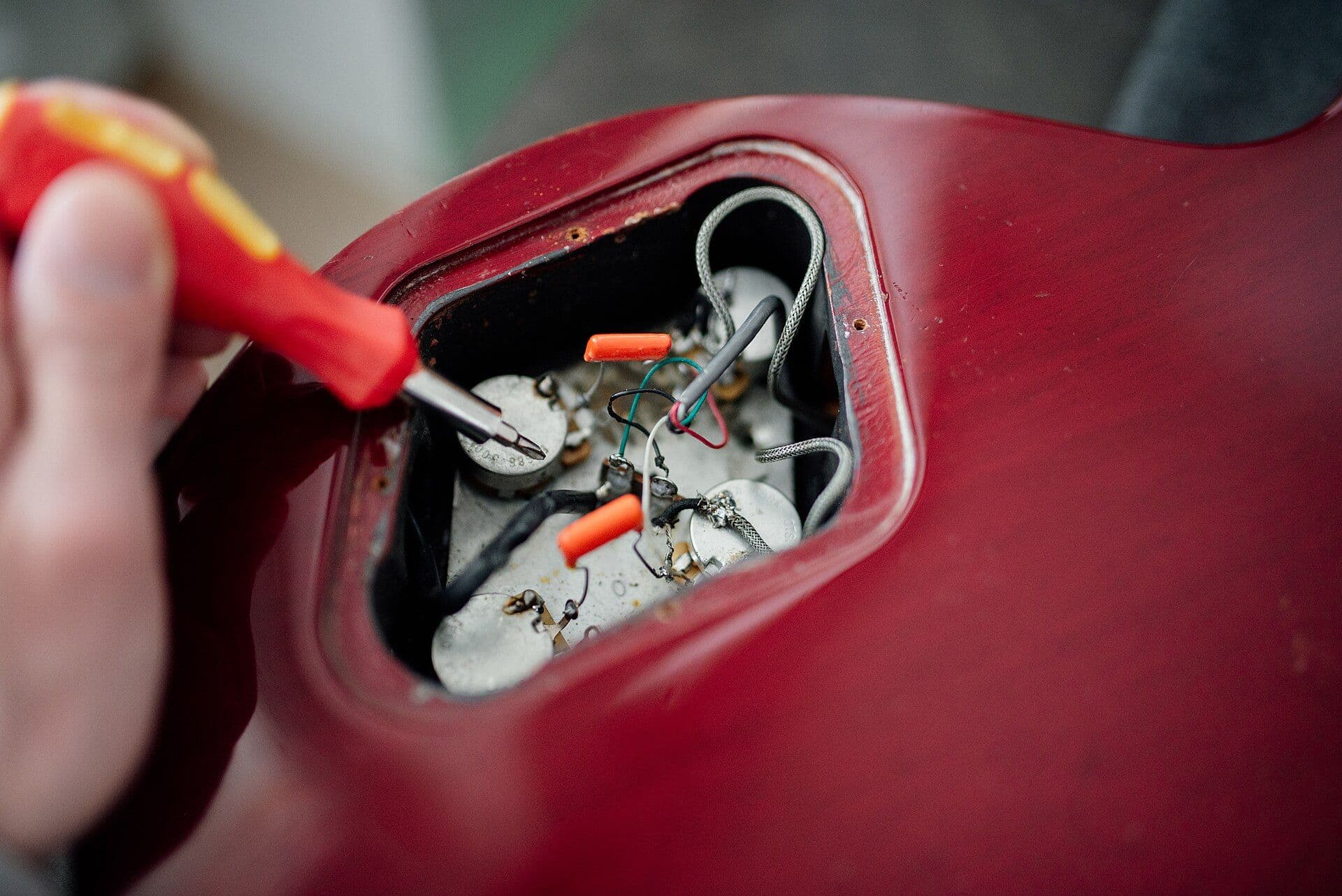Kırmızı gövdeli bir cihazın açılmış elektronik bölmesinde potansiyometre ve kablolar üzerinde çalışan bir tornavida.